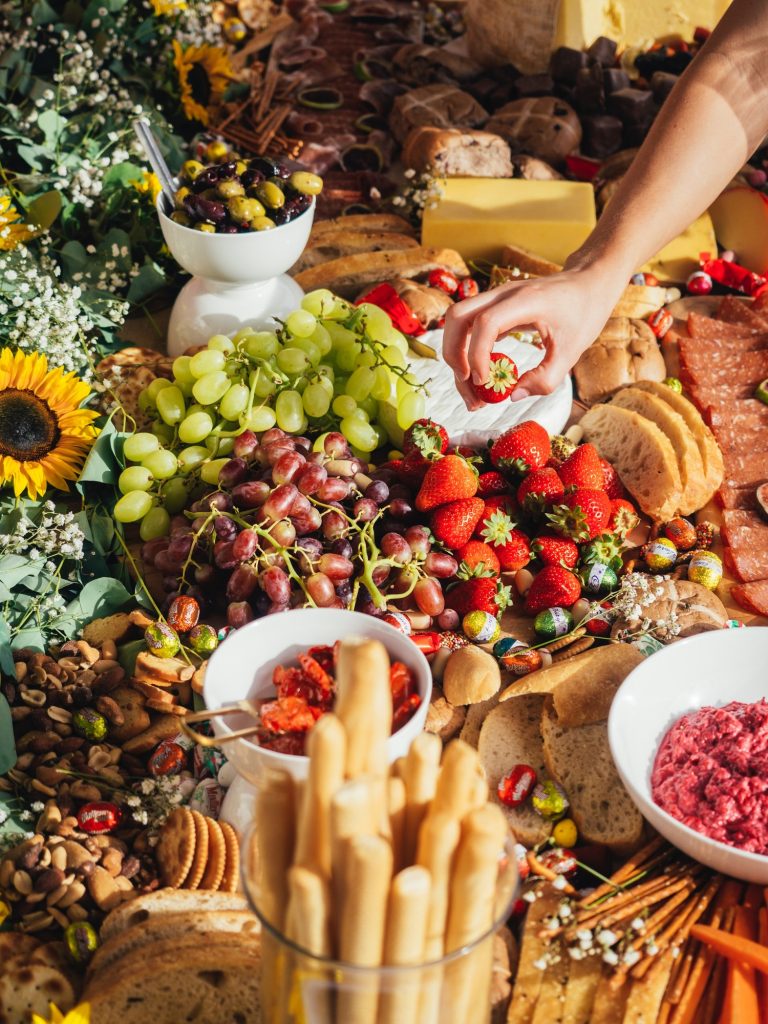 a woman's hand holding strawberry above a table filled with different foods